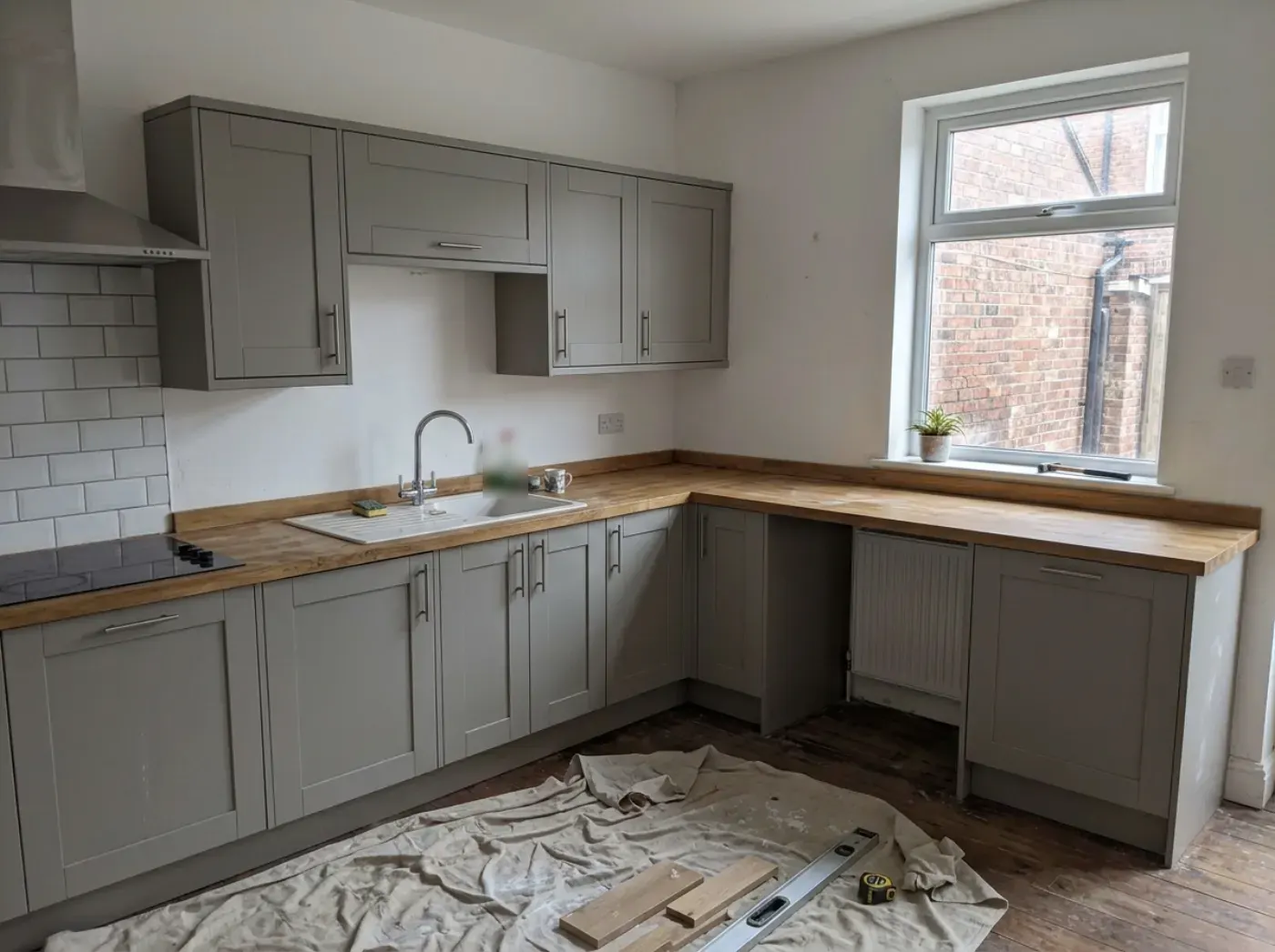 A newly fitted L-shaped kitchen with grey painted doors and an oak worktop, dust sheet still on the floor