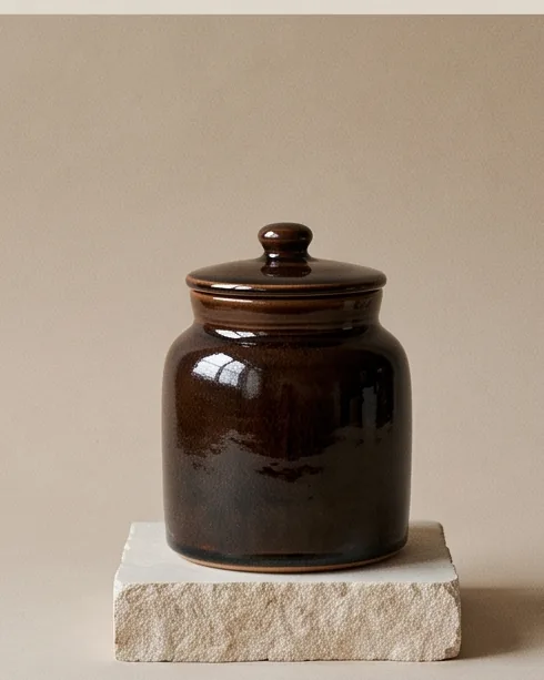 Lidded jar in a glossy dark brown tenmoku glaze on a stone plinth