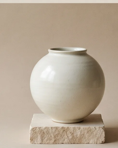 Round moon jar in a creamy white glaze on a stone plinth