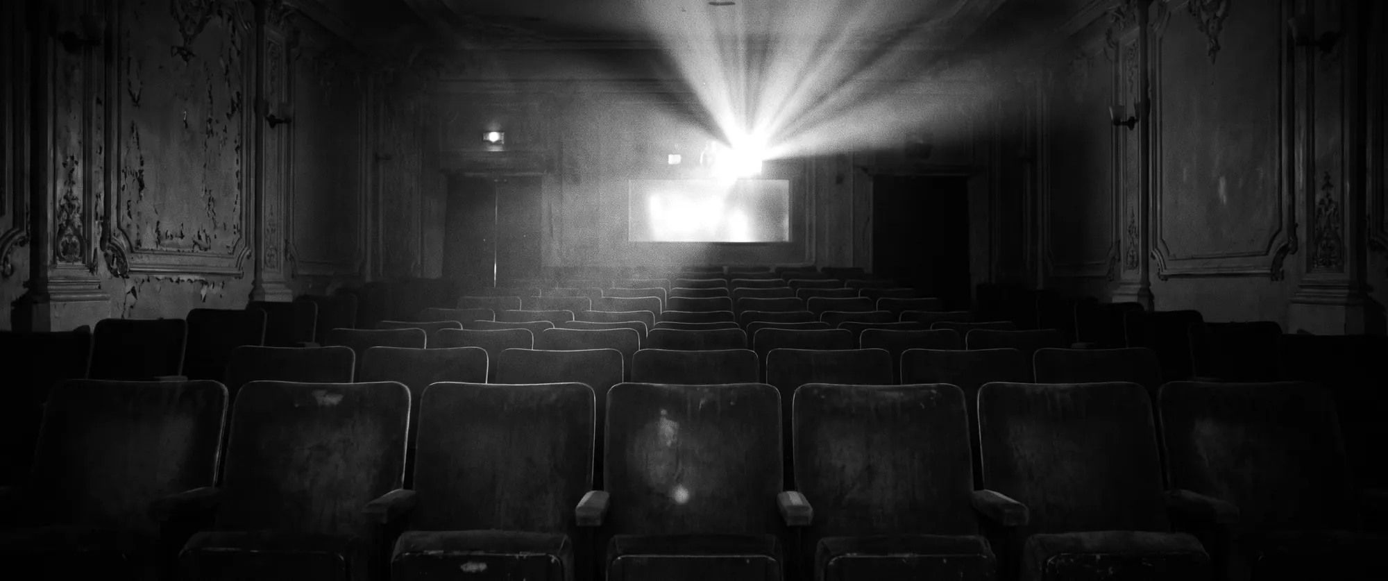 Empty velvet seats in a small old cinema, a projector beam through the dust