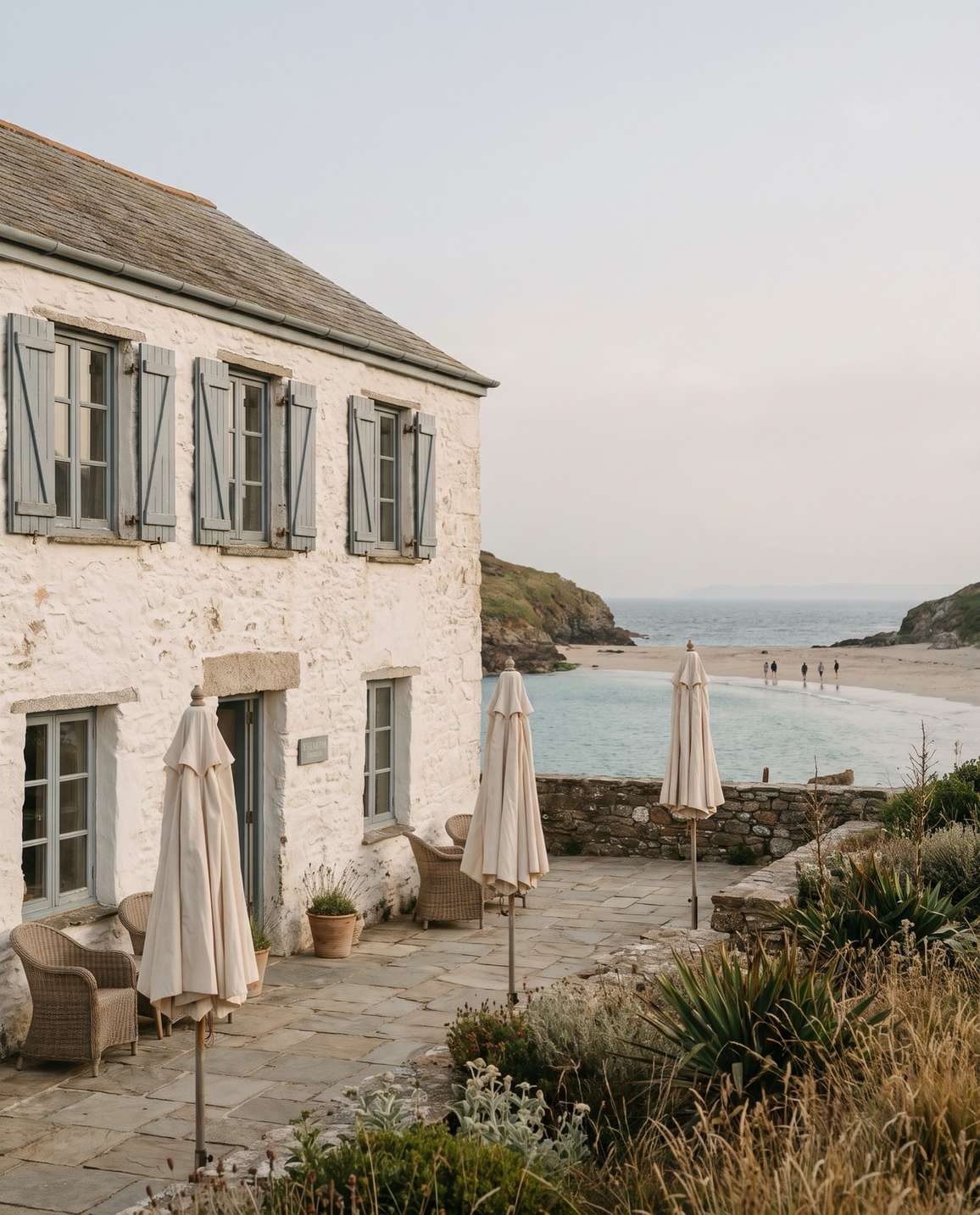 A whitewashed hotel with shutters above a quiet sandy cove