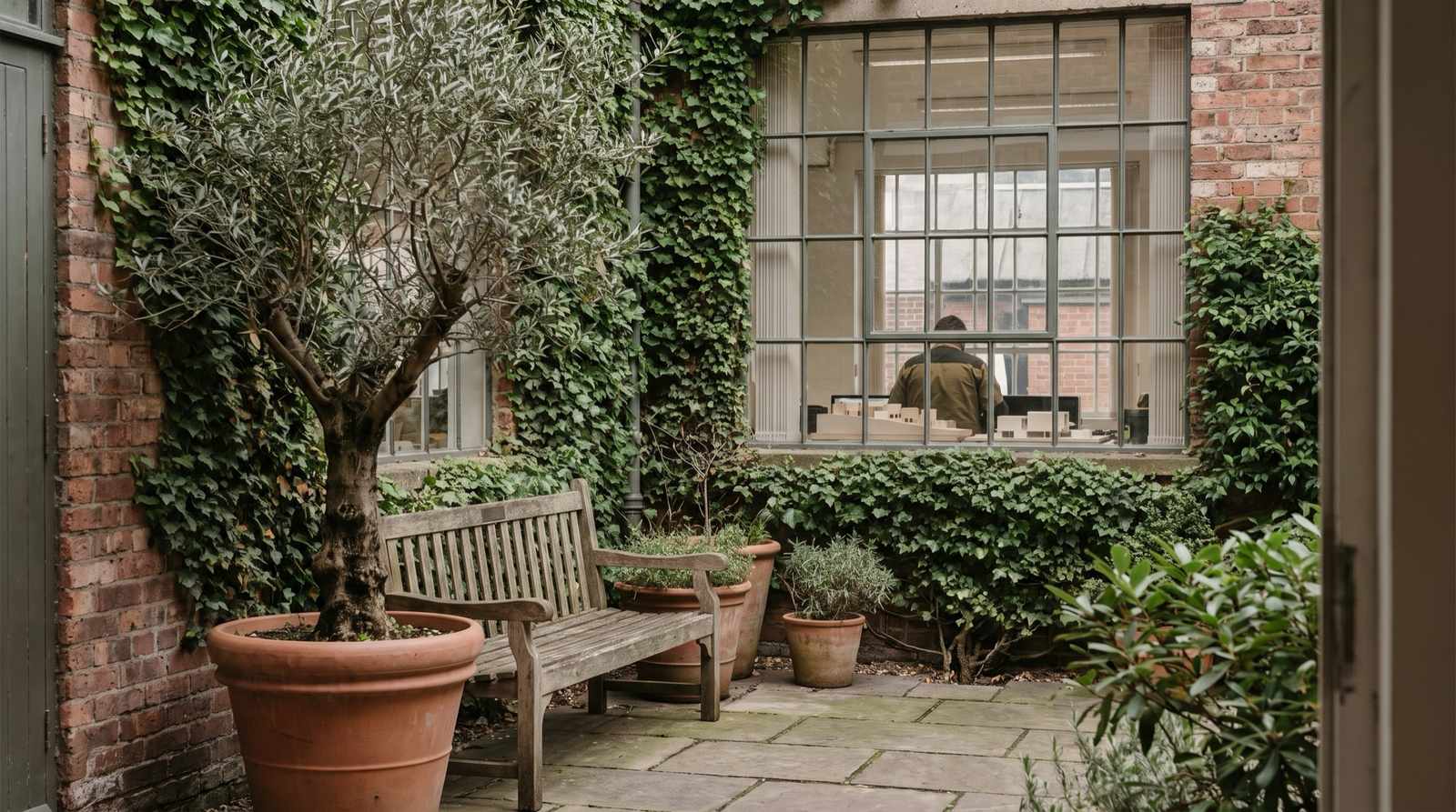 A brick courtyard with a bench and a potted olive tree